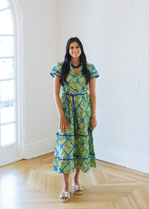Woman in a colorful dress standing in a bright room with large windows.