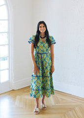 Woman in a colorful dress standing in a bright room with large windows.