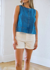 Woman wearing a blue denim top and beige shorts against a white wall.