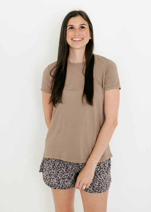 Woman wearing a beige t-shirt and patterned shorts on a white background