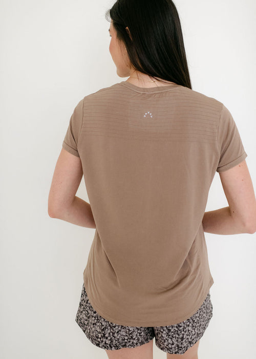Woman wearing a brown t-shirt and patterned shorts on a white background