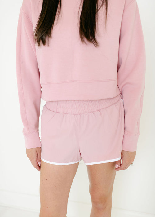 Person wearing a pink sweatshirt and shorts set on a white background