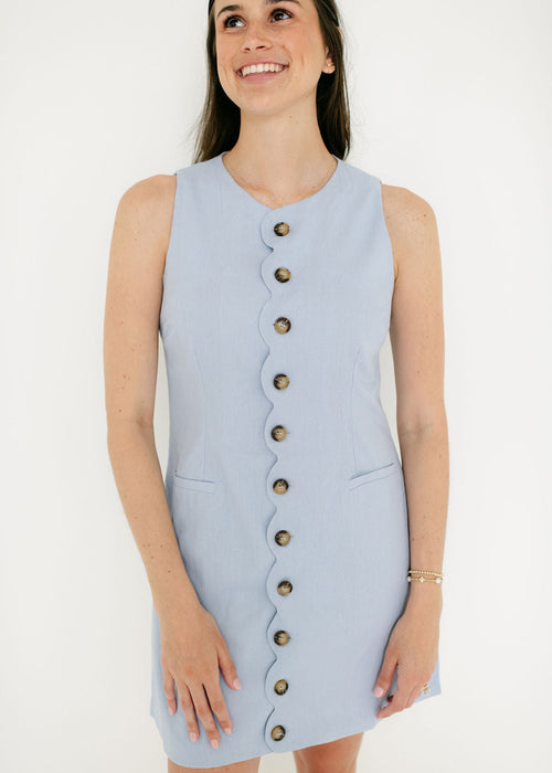 Woman wearing a light blue sleeveless dress with buttons on a white background