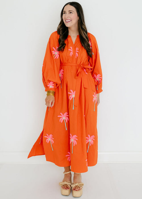Woman wearing an orange dress with pink palm tree patterns on a white background