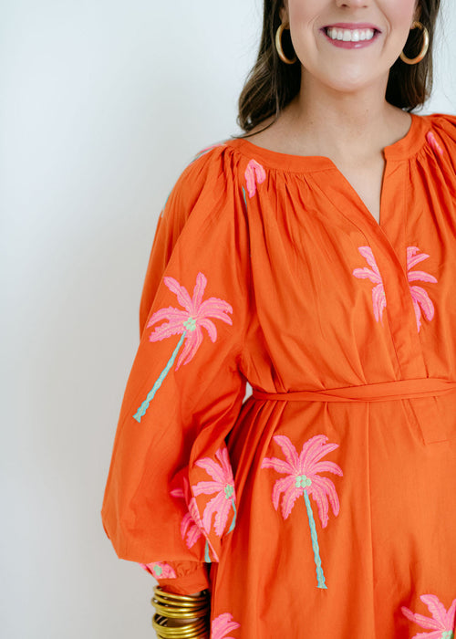 Woman wearing an orange dress with pink palm tree designs against a white background