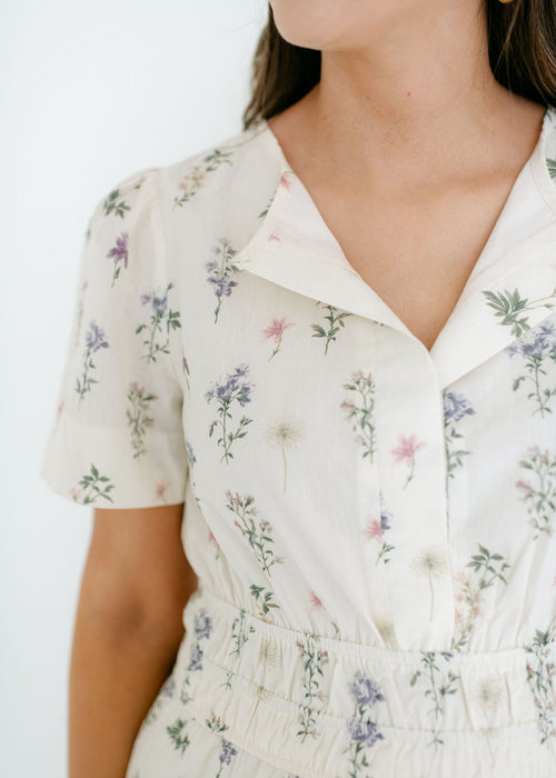 Close-up of a person wearing a white floral dress against a plain background