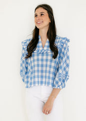 Woman wearing a blue and white checkered blouse with ruffled sleeves on a white background