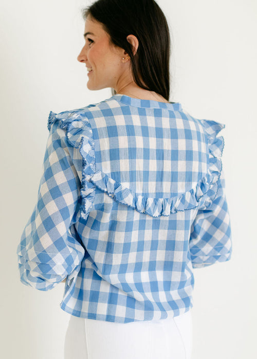 Woman wearing a blue and white checkered blouse with ruffled sleeves on a white background