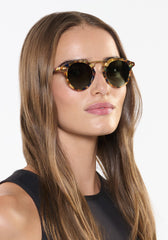 Woman wearing round sunglasses with a neutral background