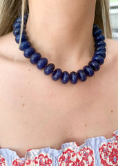 Person wearing a blue beaded necklace with a patterned top