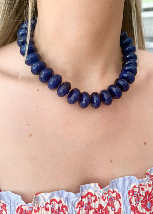 Person wearing a blue beaded necklace with a patterned top